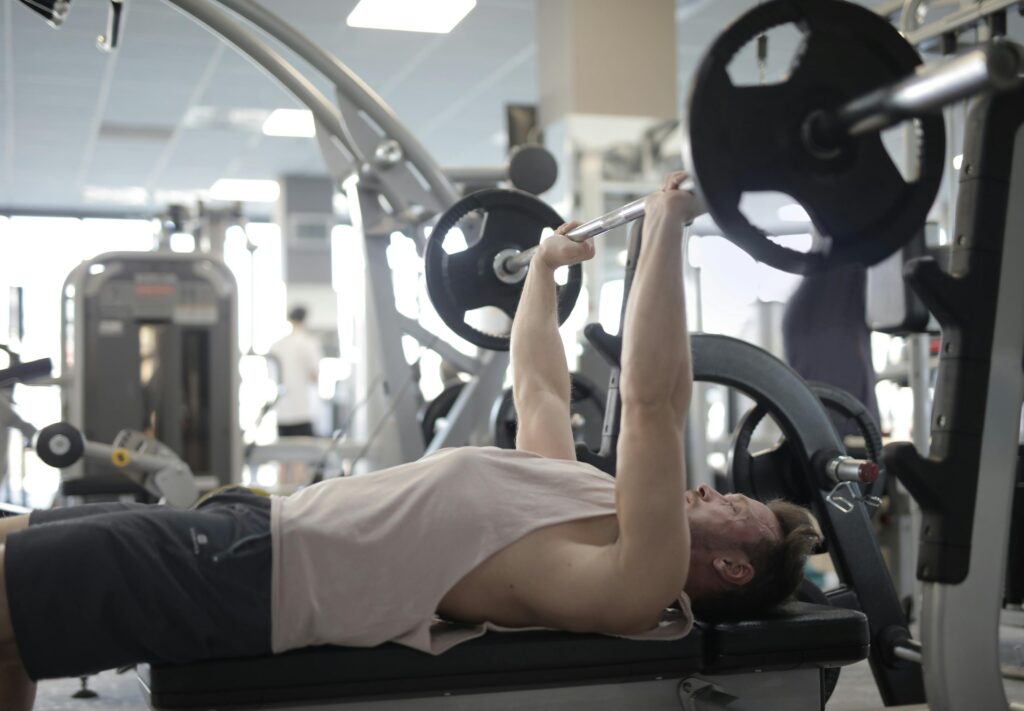 Adult man performing bench press in a gym, focusing on strength and fitness.