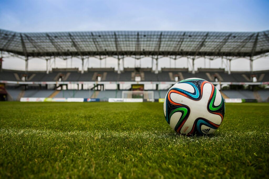 Close-up of a soccer ball on a lush grass field with an empty stadium in the background.