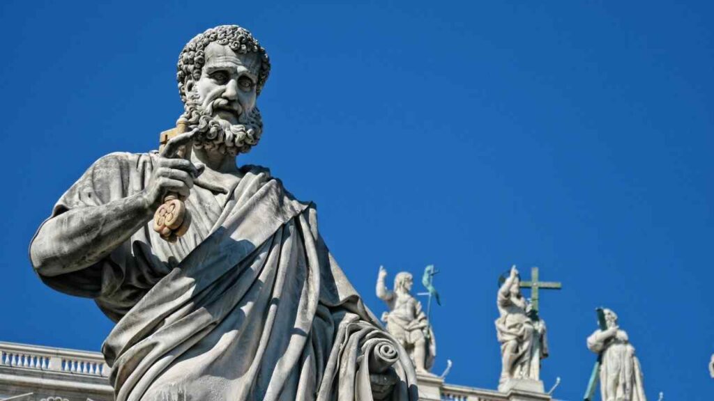 Marble statue of an ancient philosopher symbolizing Aristotle, the Father of Political Science, standing against a clear blue sky with historic figures in the background.